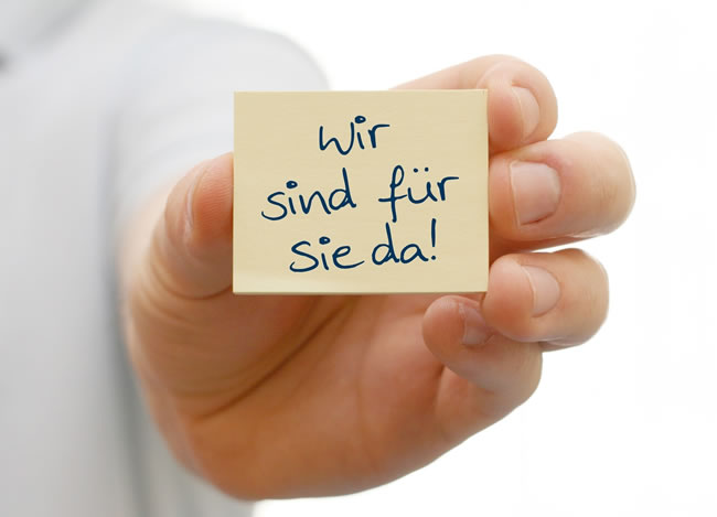 Hand hält einen Zettel mit „Wir sind für Sie da!“